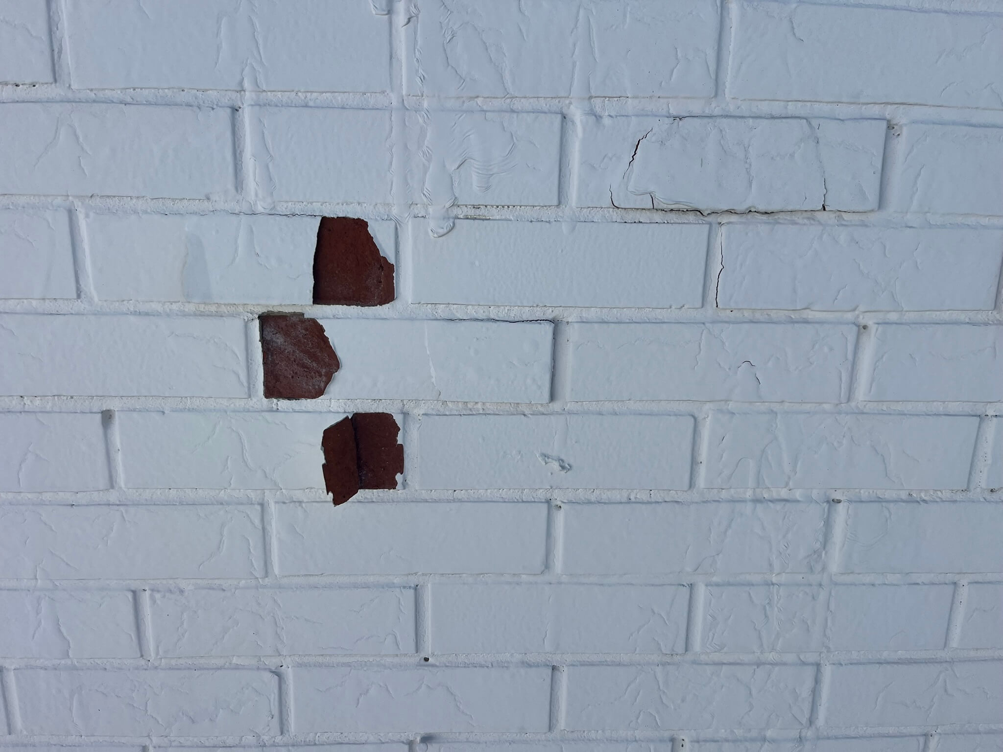 A brick wall painted in white that started peeling from a bad paint job.
