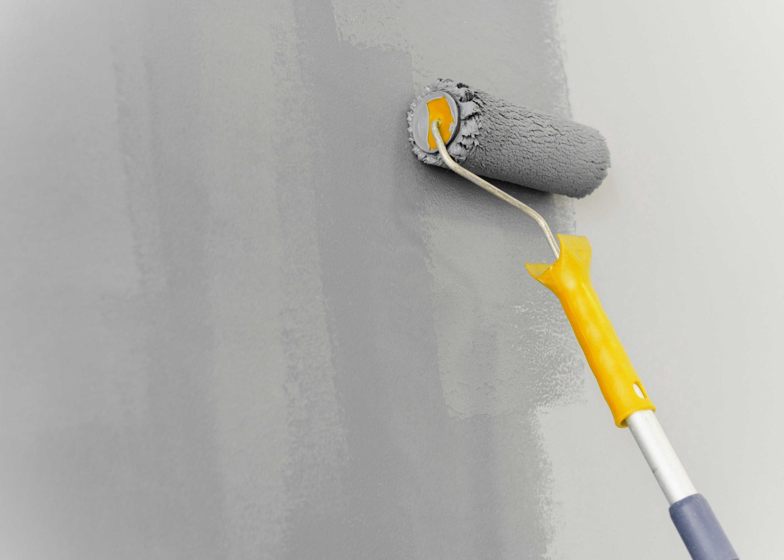A wall with damaged drywall that's been repaired and now getting a gray paint rolled on.